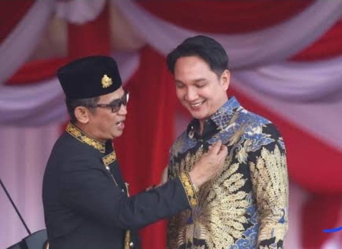 Wali Kota Rahmad Ma’sud memperhatikan dan merapikan pin HIPMI di baju batik Adam.
